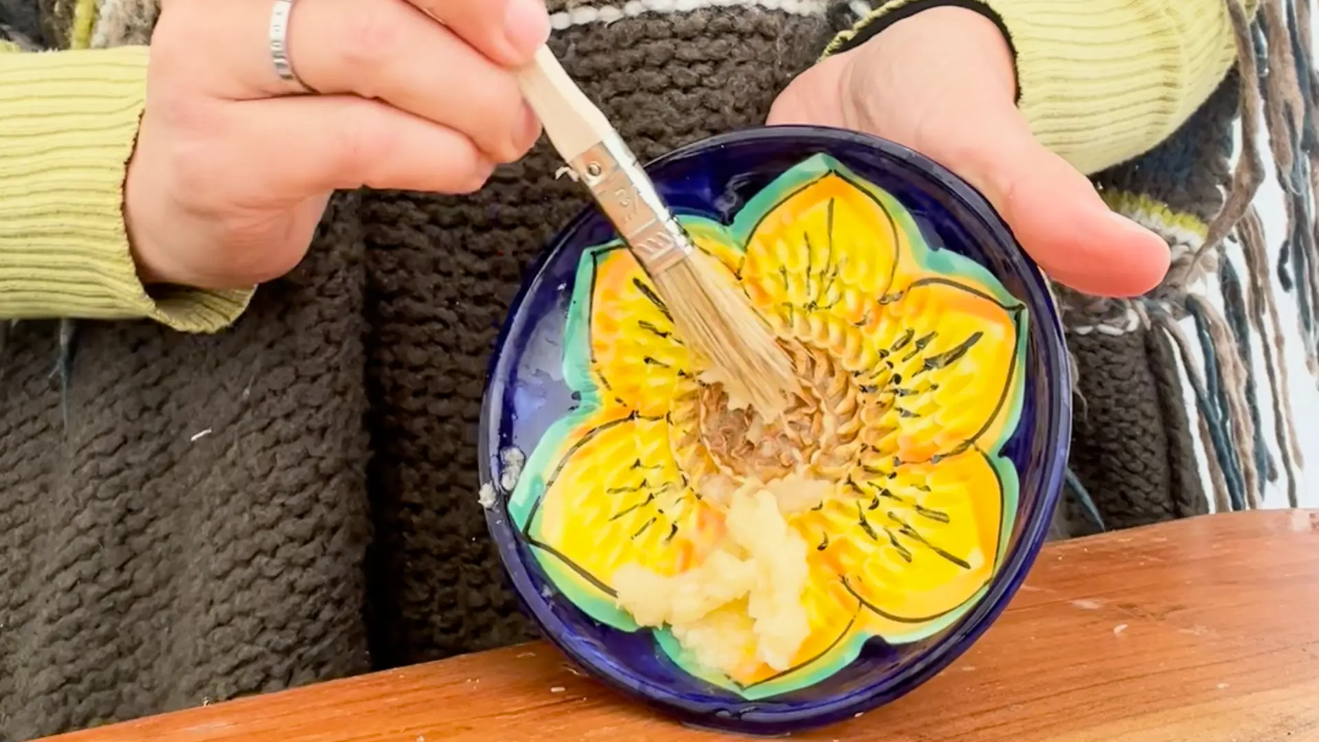 Garlic being grated into a paste with olive oil on a ceramic plate