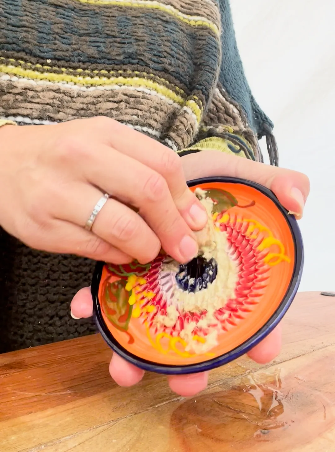 Hands grating fresh ginger into a pale paste on a hand-painted ceramic plate